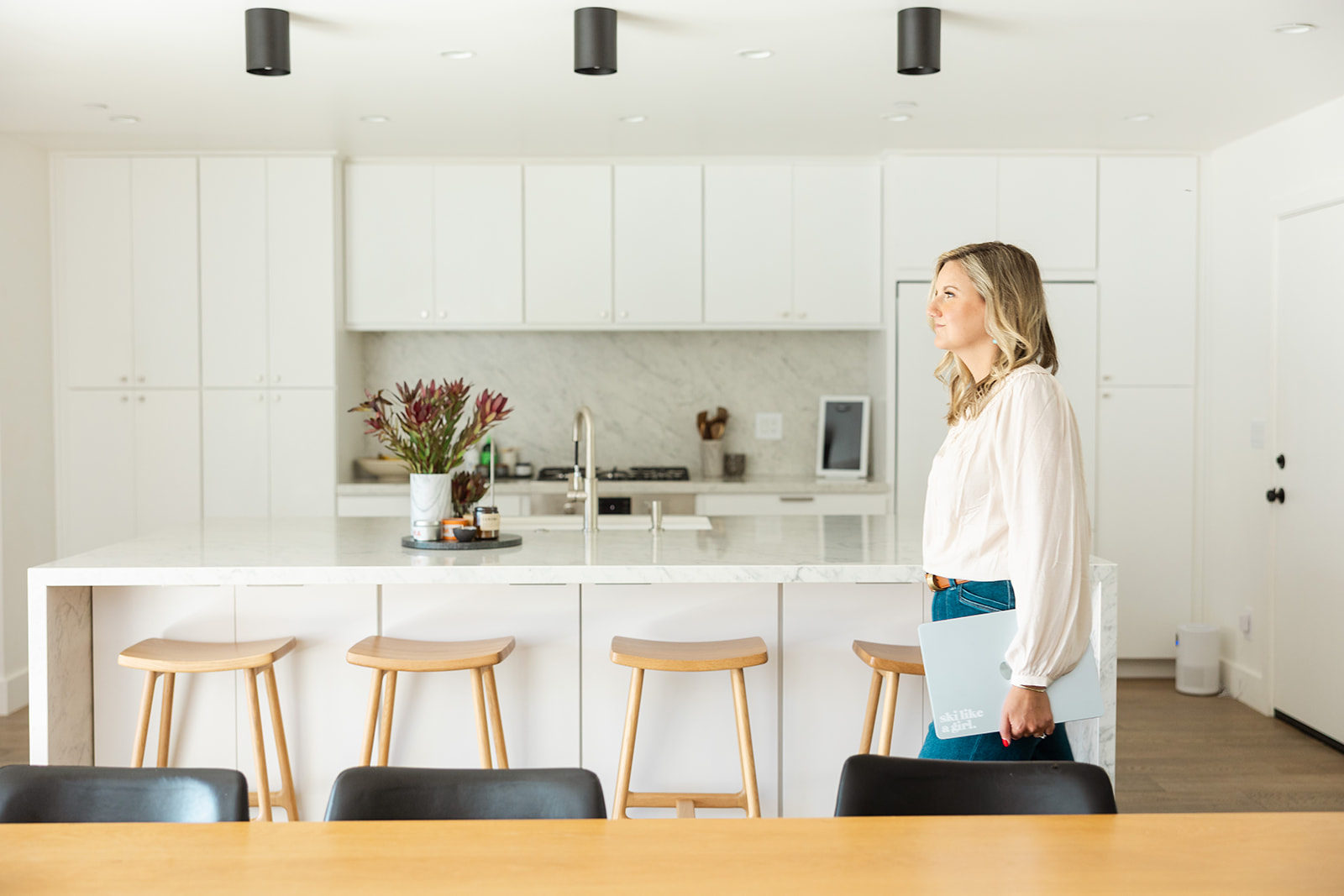 woman walking through kitchen holding laptop